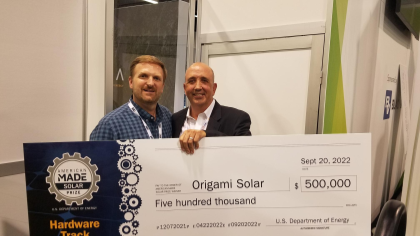 Two people stand holding a large check for five hundred thousand dollars