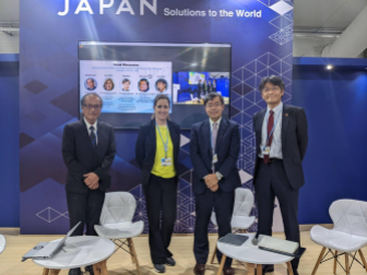 Four people smiling and standing in front of a wall reading "Japan Solutions to the World."