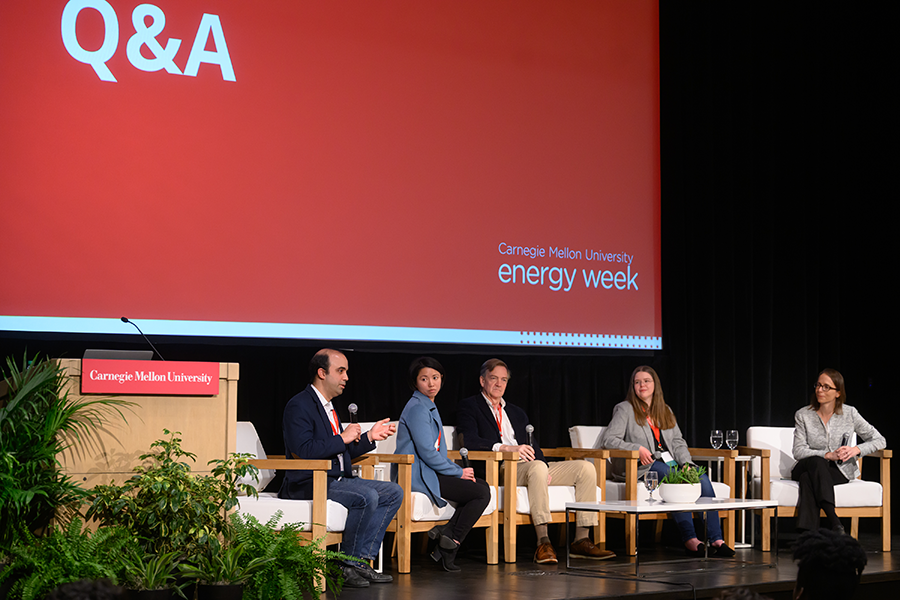 A panel of two men and three women in front of the Energy Week banners